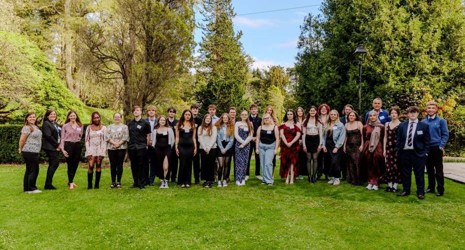 A group of young people stood together on a lawn in front of tall trees