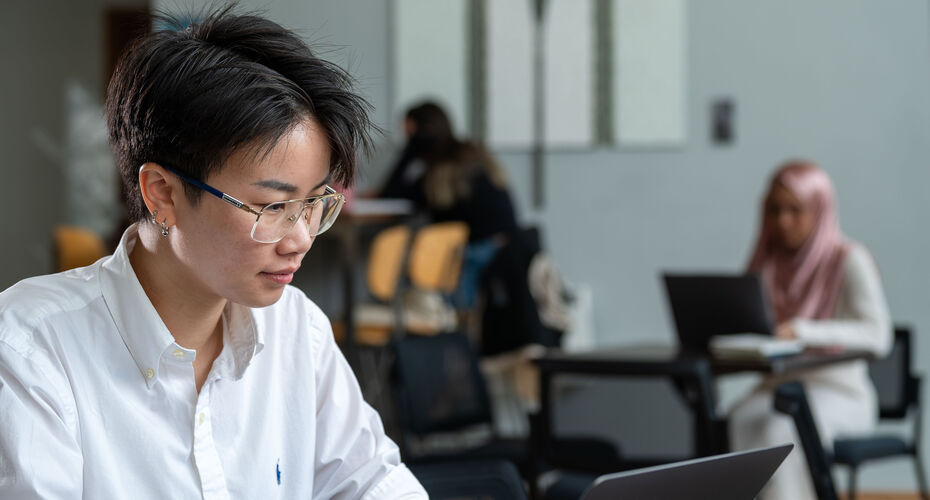 A person in a white shirt is looking down at a laptop